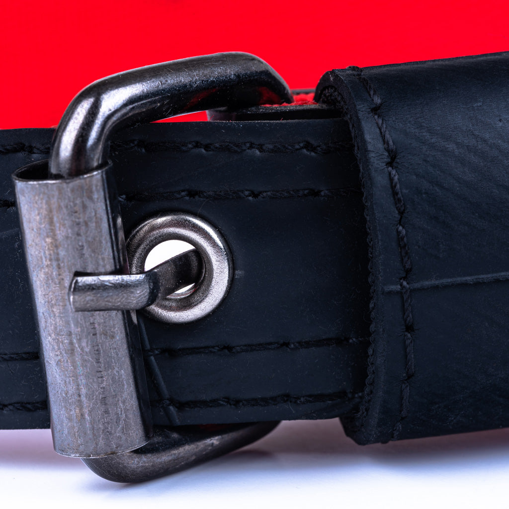 Close-up of a black leather belt with a silver buckle against a red background